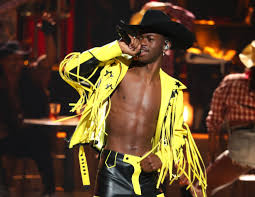 lil nas x performing on stage with a yellow opened shirt